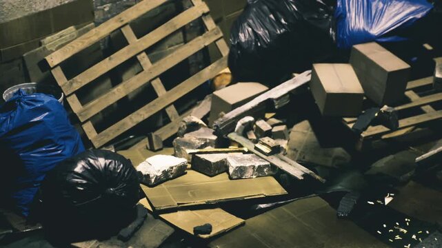 Amidst piles of black garbage bags and broken pallets, an abandoned area tells a silent story of neglect and past use. Cardboard boxes and scattered debris hint at former lives.