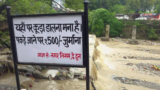 No littering sign in hindi language near a polluted stream with plastic debris pollution