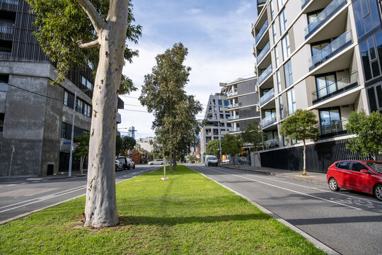 A quiet road lined with residential apartment buildings and a central grass median strip in West Melbourne, Victoria, Australia. Modern suburban neighborhood in an inner-city suburb.