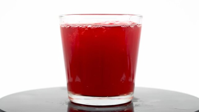 Vibrant red juice or refreshing soda drink in a clear glass isolated against a white studio background, showing effervescence and bubbles on the surface.