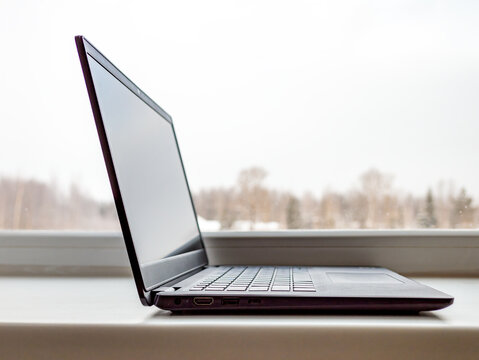 Open dark grey laptop with keyboard and ports on windowsill.