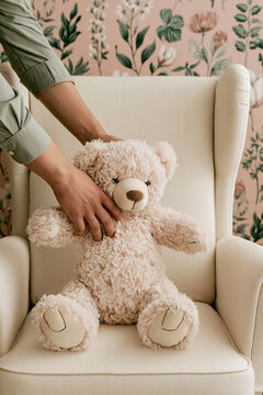 Soft teddy bear being placed on a white armchair in a nursery with floral wallpaper featuring pink and green tones