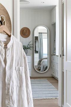 Softly blurred linen shirt hanging in a modern coastal walk-in closet with a full-length mirror and warm white walls illuminated by morning light