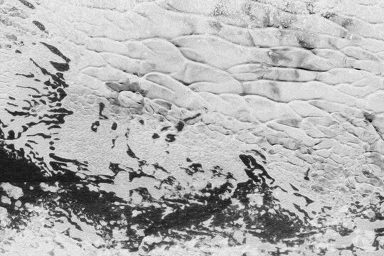 Abstract monochrome aerial view showing rhythmic ocean waves rolling toward dark coastal shoreline sandy beach textures