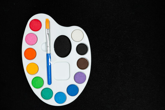Top View of Watercolor Paint Palette with Brush on Black Textured Background