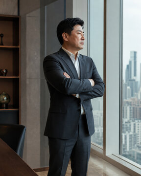 Confident asian businessman looking through window with ambitious expression