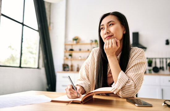 Thoughtful woman writing at a home desk.