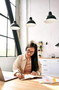 Young woman writing notes at home with laptop.