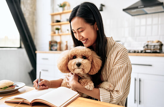 Woman writing with dog in the kitchen.