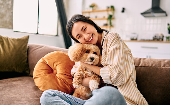 Young woman cuddling small dog on sofa at home.