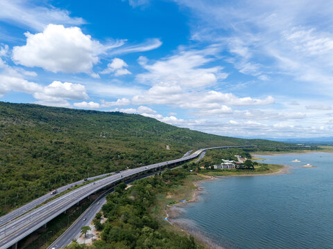 Drone aerial view of a highway running beside a reservoir with lush green mountains, Transportation infrastructure and renewable energy concept