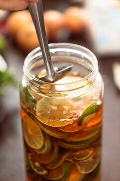 Hand stirring fresh lime slices in a glass jar filled with honey during homemade honey lime infusion preparation. Healthy drink, natural ingredients, and food preservation concept