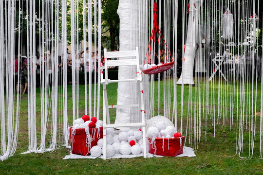 art installation features a white chair surrounded by baskets of white and red yarn, fiber art with common objects. The display utilizes a distinct red and white color scheme