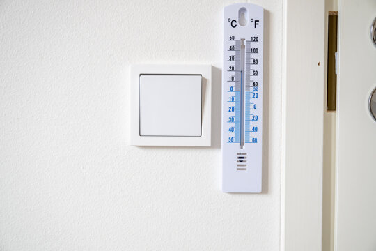 Indoor wall thermometer beside light switch for monitoring home temperature in celsius and fahrenheit