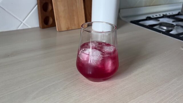 Pouring clear sparkling water into a glass filled with ice cubes and sweet syrup, refreshing summer cocktail recipe