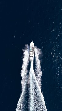 High aerial overhead view of a motor boat cruising with high speed over turquoise, sparkling ocean and passing through the picture
