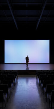 Speaker on blue illuminated stage at end of central aisle in empty auditorium. Concept of event production, keynote preparation, venue design.