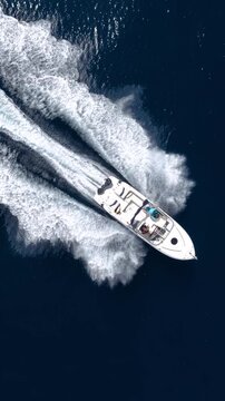 Aerial overhead tracking of a motorboat cruising with speed over the blue ocean and creating a trail of surf and waves