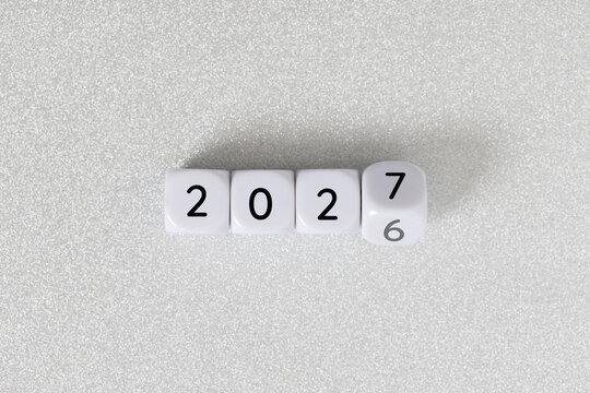 Year 2026 changing to 2027 on dice, glitter festive gray background. New year change concept