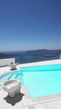 White architecture in Santorini island, Greece. Luxury swimming pool with blue water. Blue sea and the blue sky at sunny day. Travel and summer vacation concept. Vertical video
