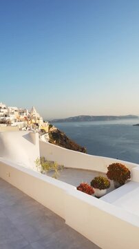 White architecture in Santorini island, Greece. Blue sea and the blue sky at sunset. Beautiful terrace with flowers. Travel and summer vacation concept. Vertical video
