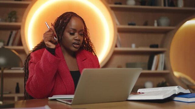 African female student having an online video lesson on laptop and taking notes