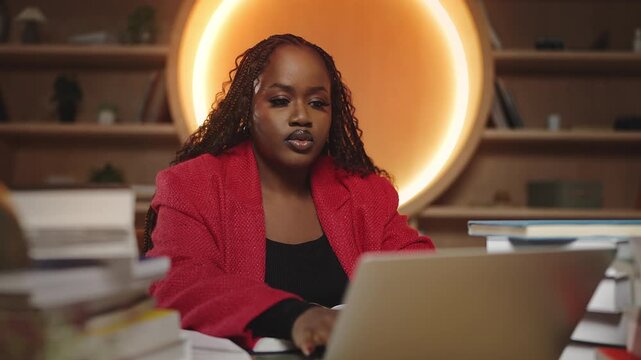 African female student doing scientific research in library, typing on laptop
