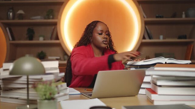 Black female student studying hard behind stacks of books in library, education