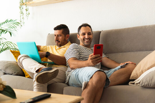 Happy gay couple relaxing at home using technology