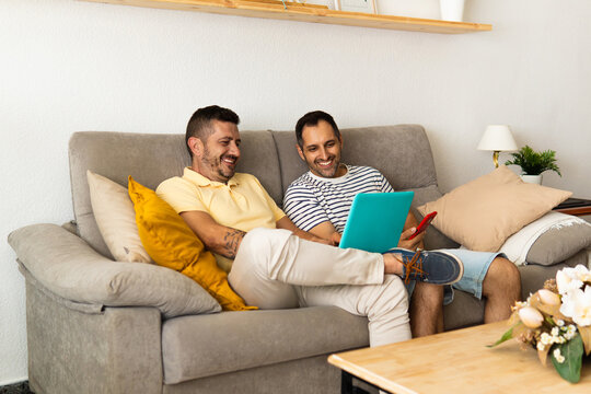 Gay couple relaxing on sofa using laptop and phone