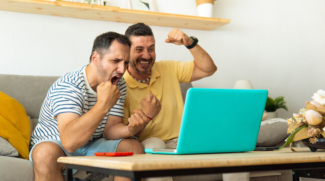 Friends celebrating victory watching online content on laptop