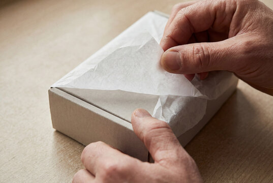 Person Unwrapping A Small Cardboard Parcel With Delicate Tissue Paper