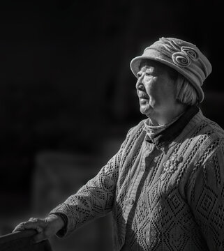 Black and white image of an elderly woman standing in the backyard and contemplating.