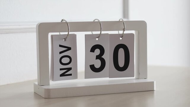 Hand flipping wooden desktop calendar from November 30 to December 1, concept of new month, year end approach, schedule planning, and time change.