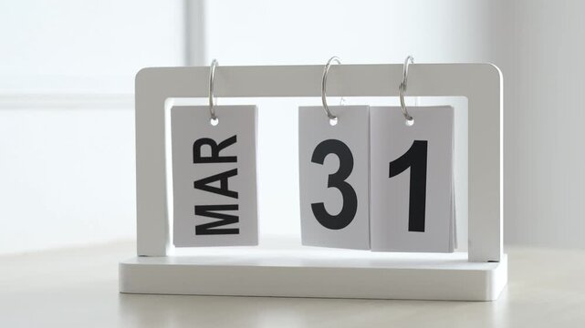 Hand flipping wooden desktop calendar from March 31 to April 1, concept of new month, April Fools Day, schedule planning, and time change.