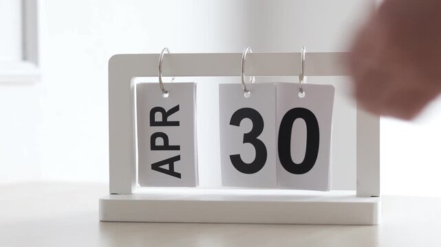 Hand flipping wooden desktop calendar from April 30 to May 1, concept of new month, labor day, schedule planning, and time change.