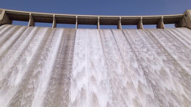 Dam spillway releasing water. Travel aerial view low-angle shot. Water discharge from the upper section of a gravity dam. Rules Dam. Spain.