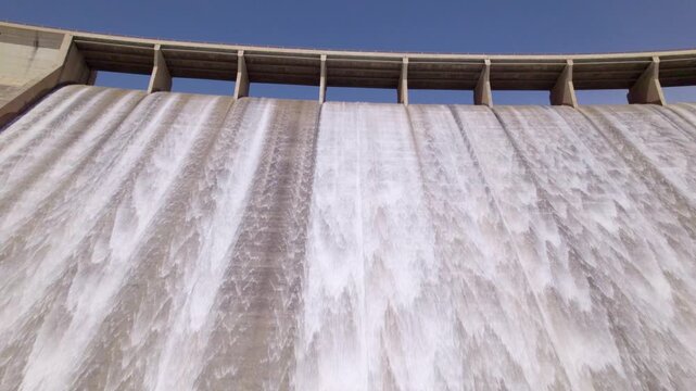 Dam spillway releasing water. Travel aerial view low-angle shot. Water discharge from the upper section of a gravity dam. Rules Dam. Spain.
