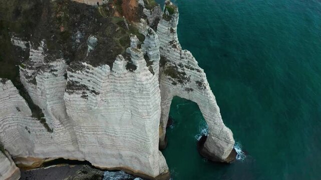 A smooth cinematic drone orbit capturing the majestic Porte d'Aval natural alabaster arch and sheer coastal cliffs in Normandy.