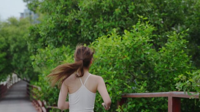 Active woman enjoys outdoor run exercise activity alone in countryside, she runs along wooden bridge boardwalk surrounded by dense green forest foliage during summer morning workout.