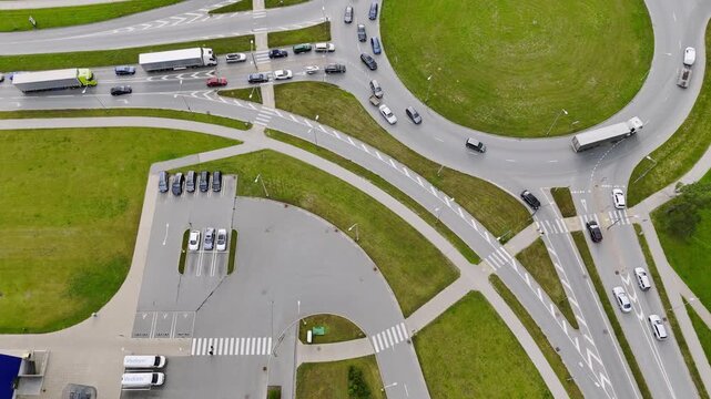 Aerial top-down view of a roundabout traffic crash involving a car with a trailer, causing cars and trucks to slow down and maneuver around the obstruction.