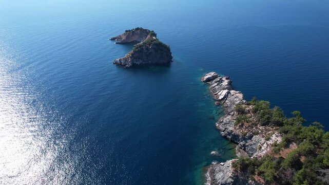 Drone aerial of a Aliki Beach secluded Mediterranean bay on Thassos, Greece with clear blue water, sandy shore, paddleboards, swimmers and stunning natural scenery.