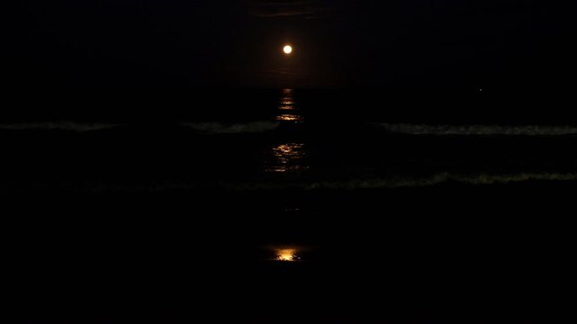 Moonlight stripe rippling over ocean surface as strawberry full moon rises