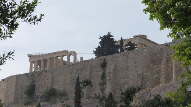 Parthenon and massive fortification walls of the Acropolis viewed from below through trees in Athens