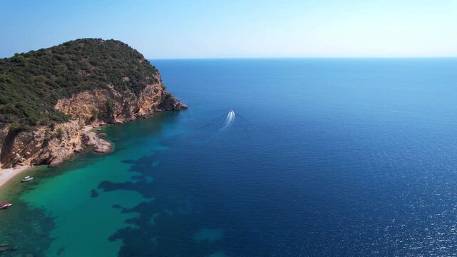Drone aerial of a Aliki Beach secluded Mediterranean bay on Thassos, Greece with clear blue water, sandy shore, paddleboards, swimmers and stunning natural scenery.
