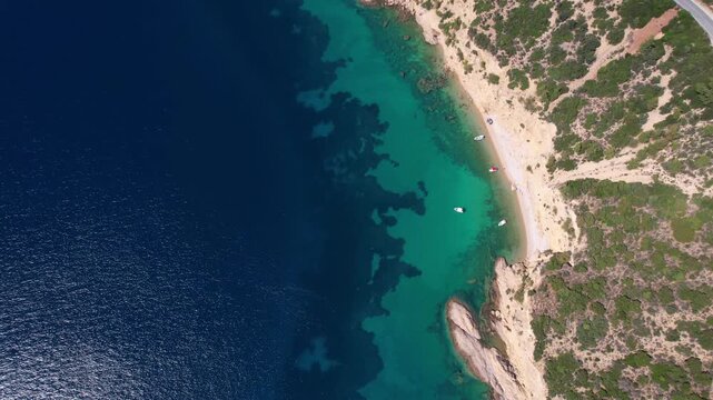 Drone aerial of a Aliki Beach secluded Mediterranean bay on Thassos, Greece with clear blue water, sandy shore, paddleboards, swimmers and stunning natural scenery.
