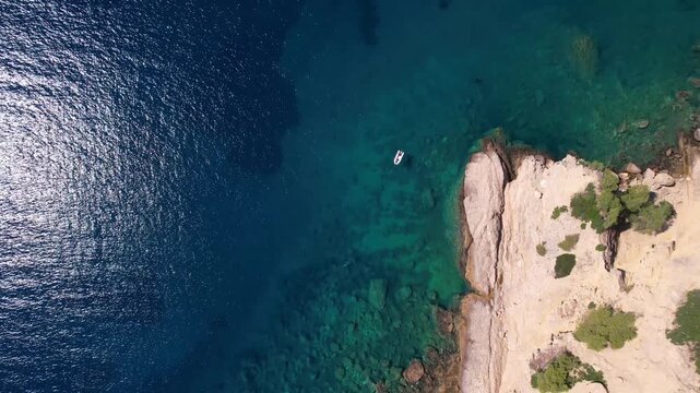 Drone aerial of a Aliki Beach secluded Mediterranean bay on Thassos, Greece with clear blue water, sandy shore, paddleboards, swimmers and stunning natural scenery.