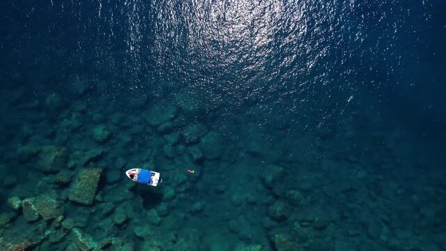 Drone aerial of a Aliki Beach secluded Mediterranean bay on Thassos, Greece with clear blue water, sandy shore, paddleboards, swimmers and stunning natural scenery.