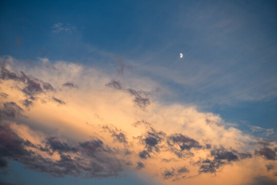 Beautiful crescent moon in blue evening sky over golden sunset clouds