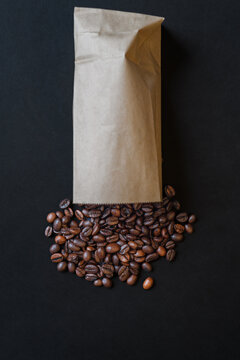 Vertical minimalist shot of coffee beans spilled from paper bag on black background